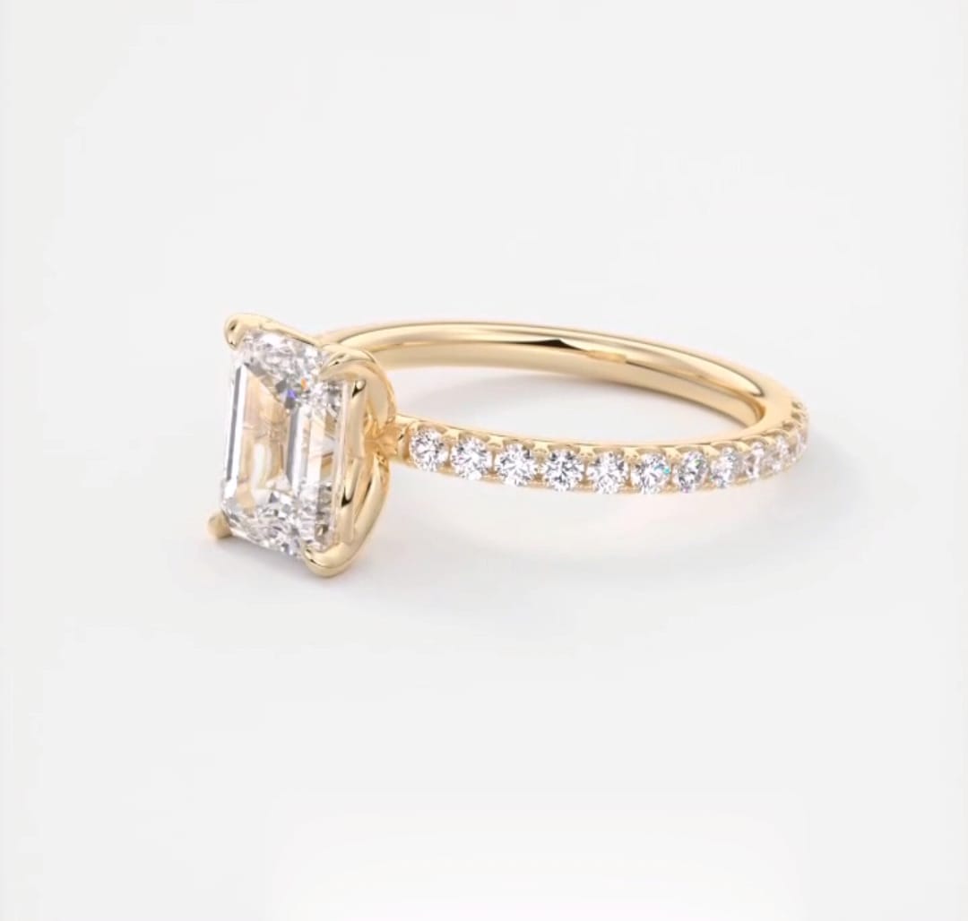 Three-quarter view of a 2 carat emerald cut lab grown diamond engagement ring in yellow gold with pavé band.