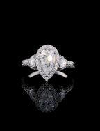 Front view of a 3 CT pear cut lab grown diamond engagement ring with a halo and trillion side stones on a black background