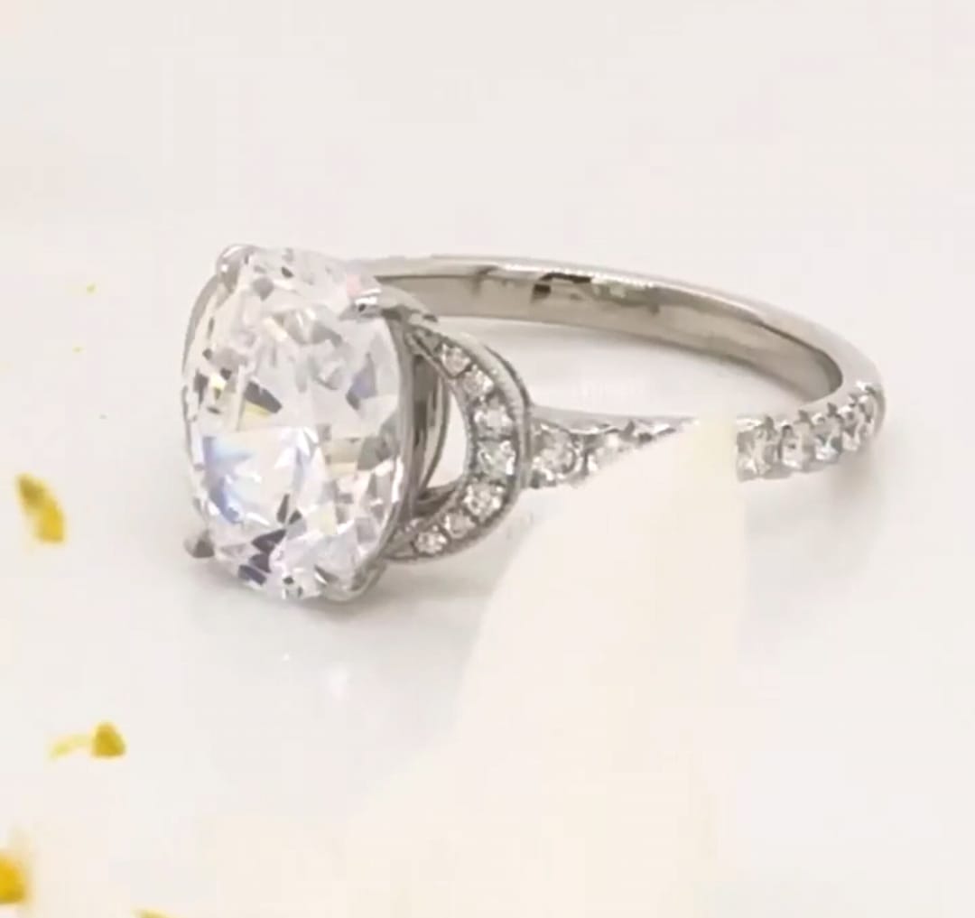 Side angle view of a 3 CT oval cut lab grown diamond engagement ring with crescent pave accents on a white surface