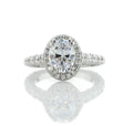 Front view of a 2 carat oval cut lab grown diamond engagement ring with milgrain halo and pavé band on a white reflective background.