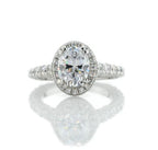 Front view of a 2 carat oval cut lab grown diamond engagement ring with milgrain halo and pavé band on a white reflective background.