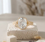 Close-up front view of an elongated cushion-cut engagement ring with a detailed filigree yellow gold band resting on a textured white stone prop.