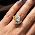 Close-up on-finger macro shot of 2 CT pear shape lab grown diamond ring with gold leaf cluster band.