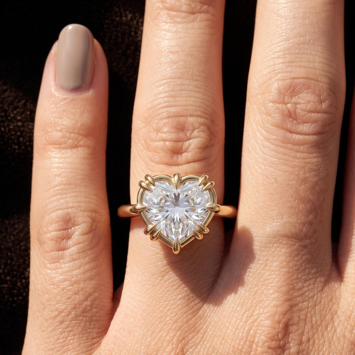 A heart-shaped diamond ring in a gold prong setting, worn on a finger. The ring is shown in close-up 