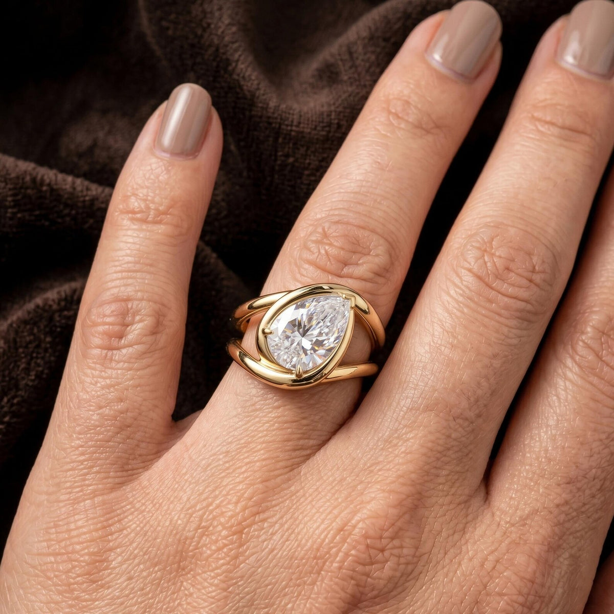 Extreme close-up of a 2 carat pear shape lab grown diamond in a modern organic bezel setting held between fingers.