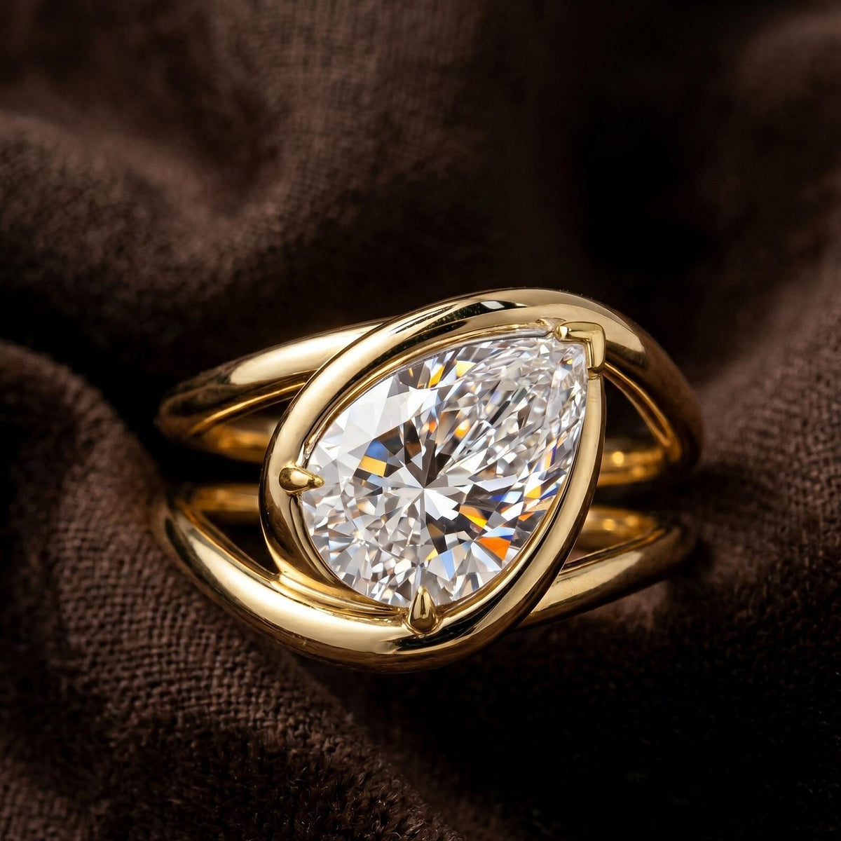 A gold ring featuring a large pear-cut clear gemstone in a prong setting, resting on a dark brown textured fabric background.