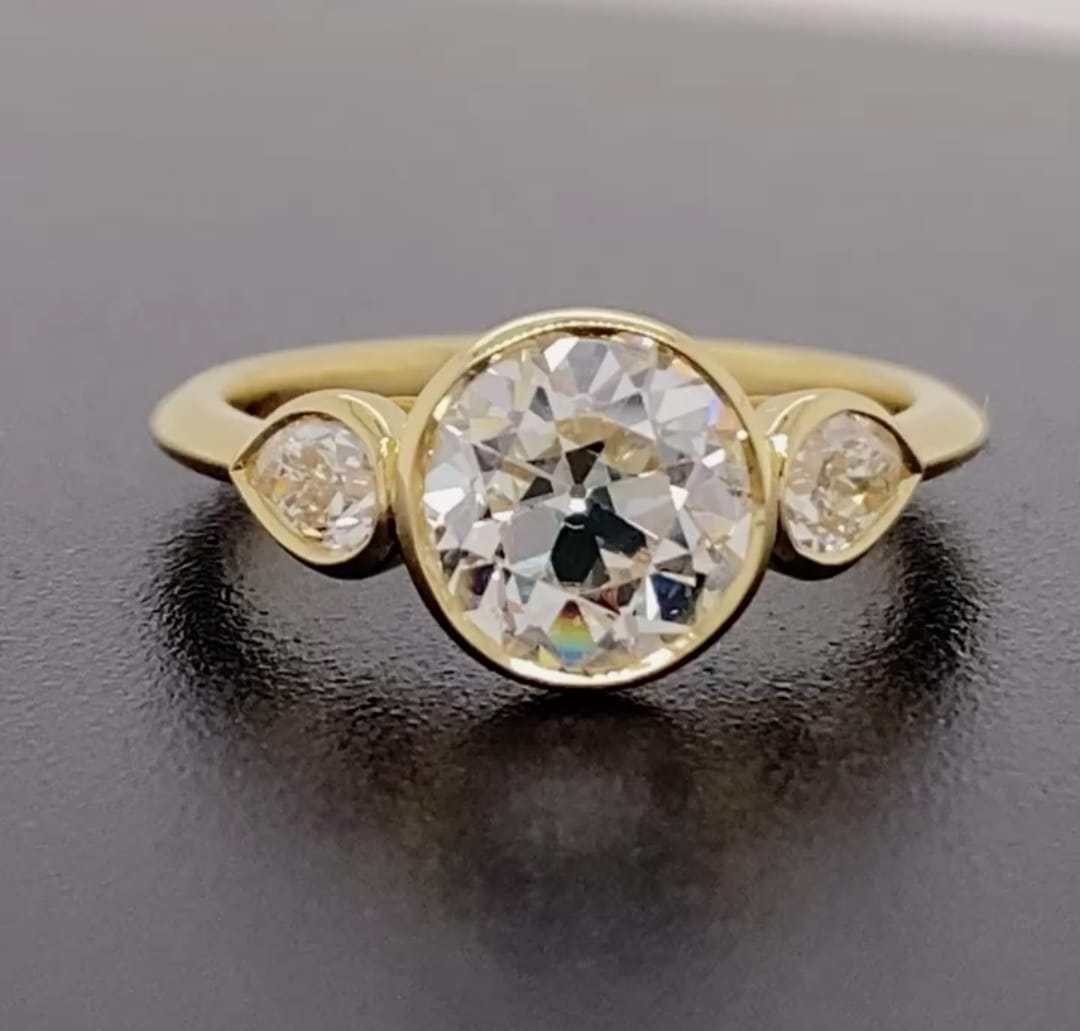 Front top view showing a 3 CT round bezel-set lab diamond ring flanked by two pear side diamonds.