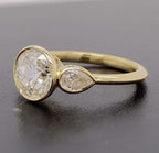 Close-up of the pear cut side stone bezel setting on a yellow gold lab grown diamond ring.