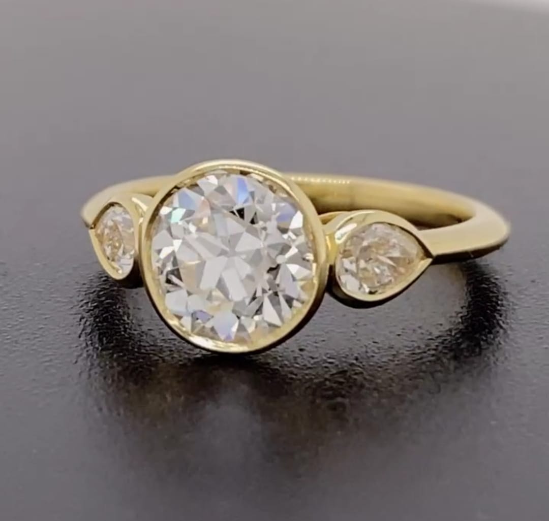 Angled view of a modern 3 carat round cut lab diamond three stone ring in bezel setting.