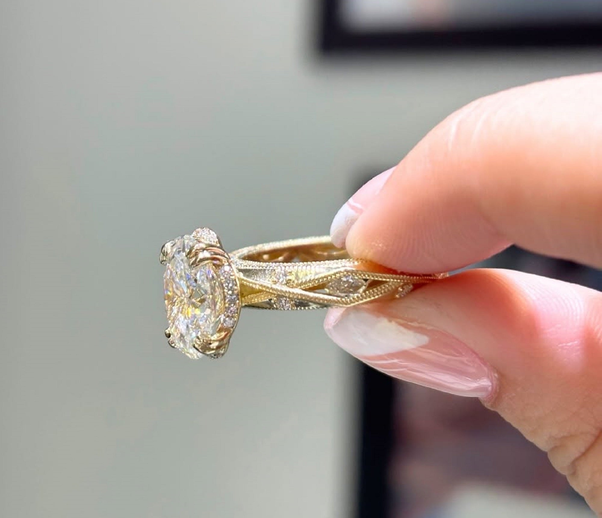Side angle view of a yellow gold engagement ring being held, showing an intricate milgrain and pave diamond band.