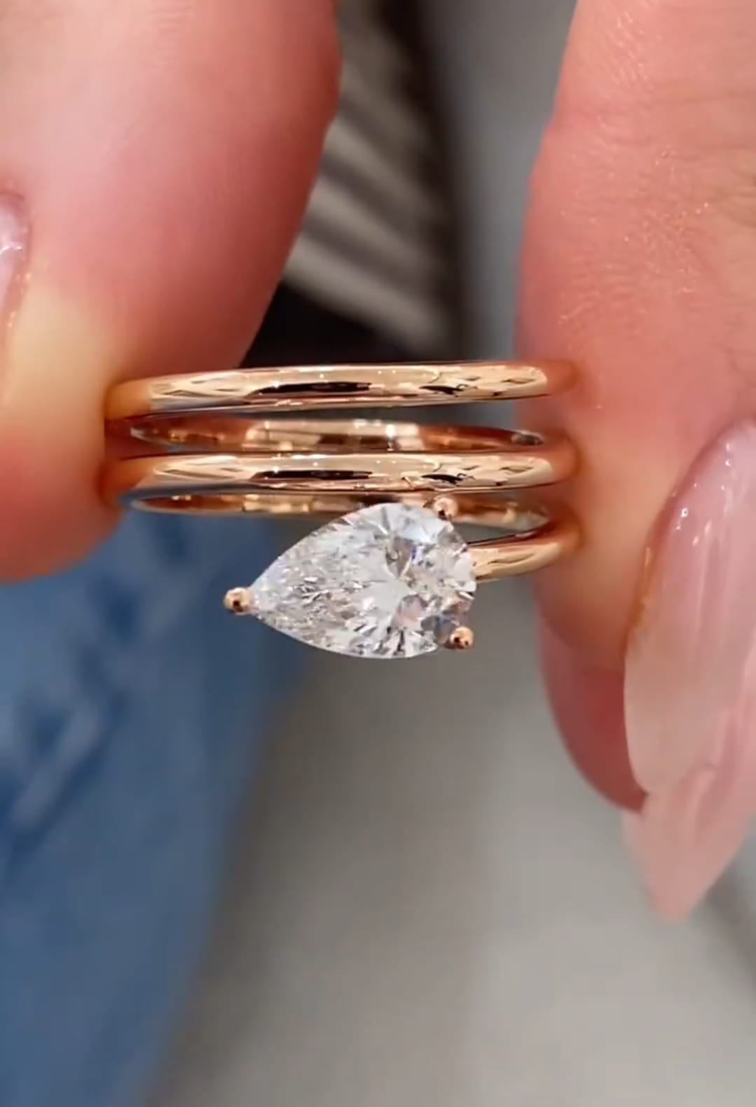 Close-up front view of a 1.5 CT pear cut lab grown diamond set on a multi-band rose gold ring held between fingers.