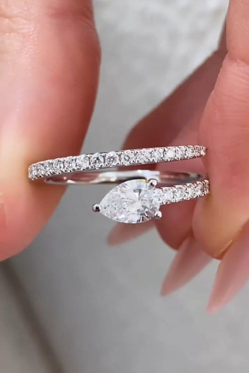 Close-up held shot of a 1.5 CT pear cut lab grown diamond bypass ring with a pave diamond band in white gold.