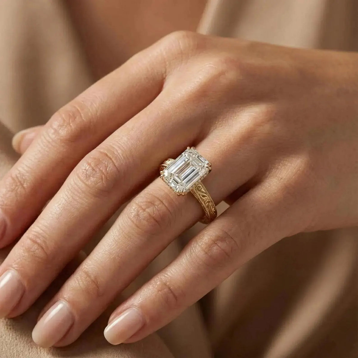 3 CT emerald cut lab grown diamond engagement ring with engraved yellow gold band shown on finger