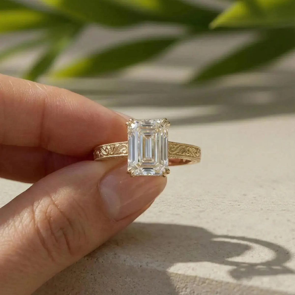 Person holding a 3 carat emerald cut lab created diamond ring with vintage engraved band
