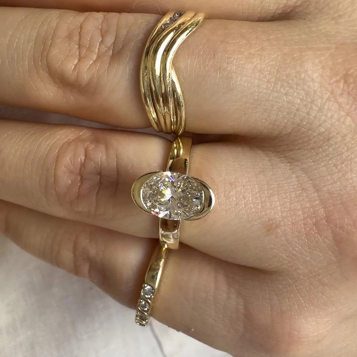 Top-down view of 2 CT oval cut lab grown diamond bezel ring worn on hand with gold stacking bands