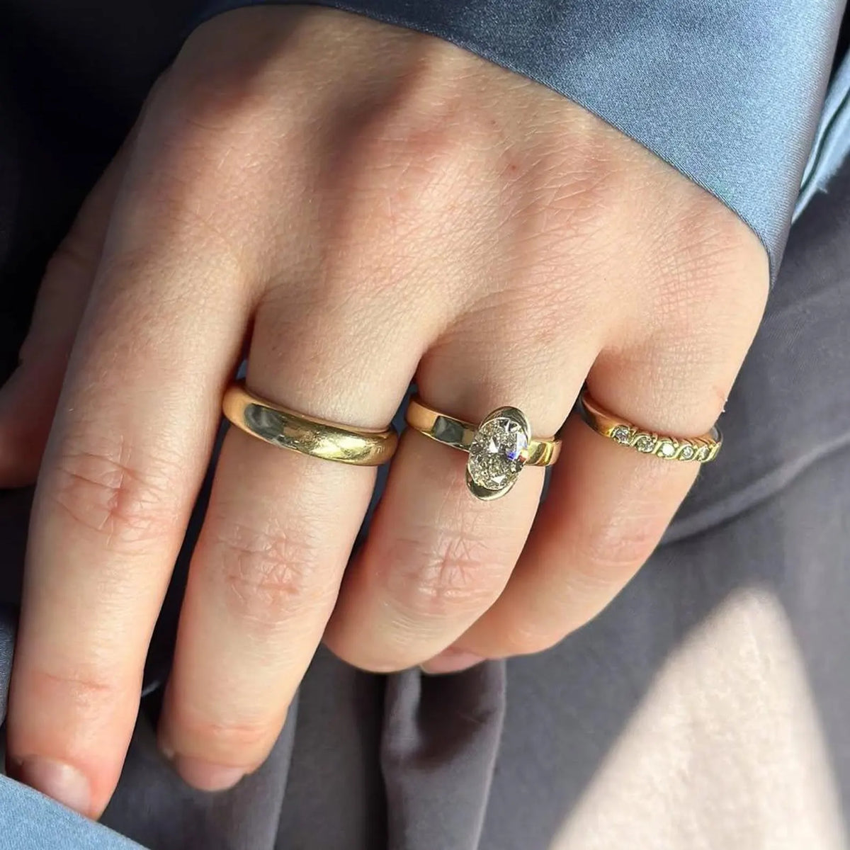 Hand wearing 2 carat oval cut lab diamond bezel set solitaire ring in 14k yellow gold