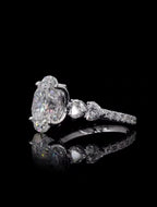 Angled view showing the 4 carat oval center diamond paired with heart cut side stones on a pave setting
