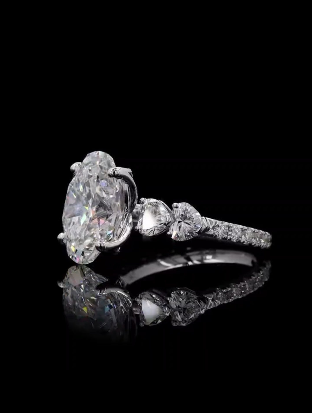 Angled view showing the 4 carat oval center diamond paired with heart cut side stones on a pave setting
