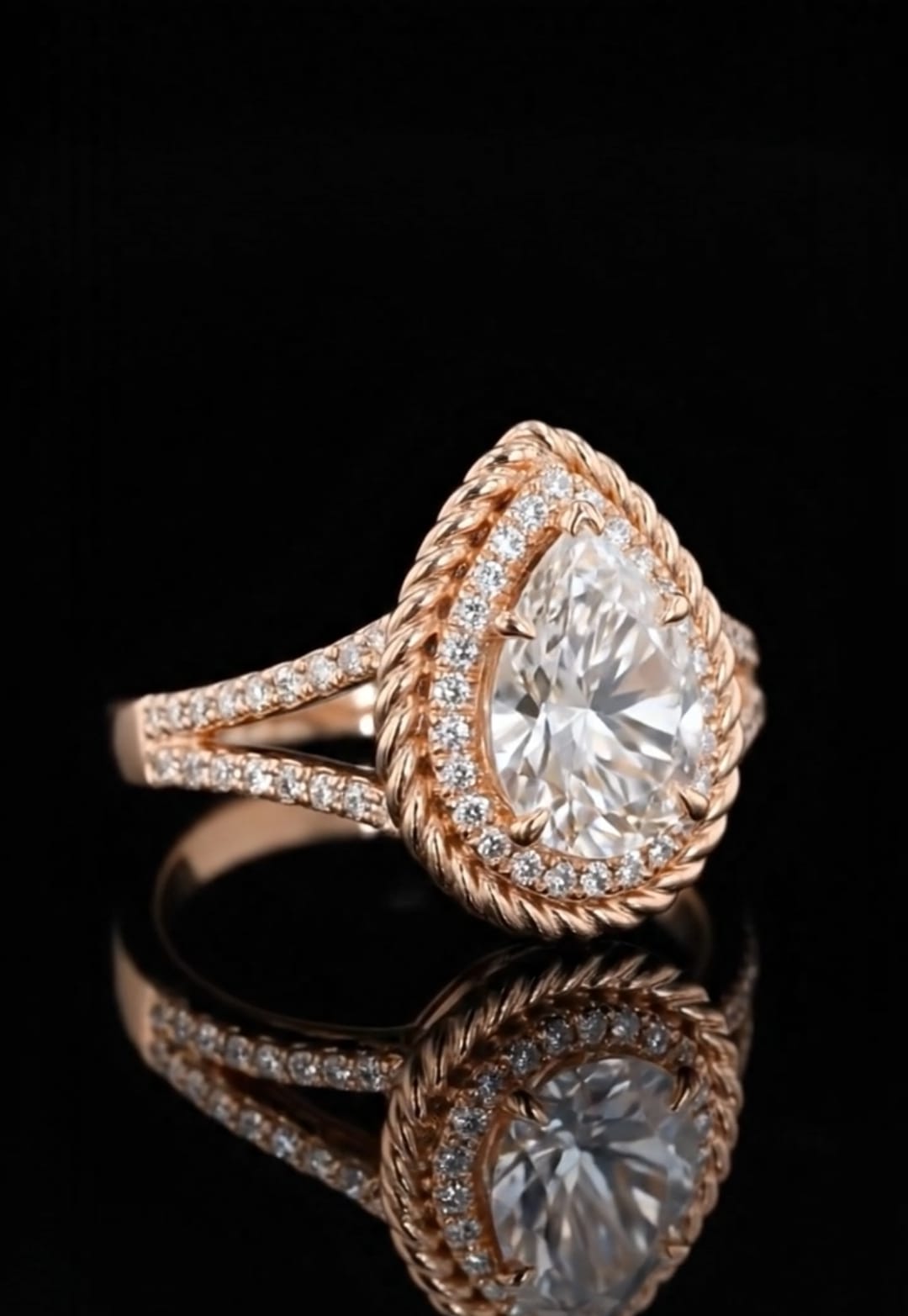 Side angle view of a rose gold pear engagement ring showing the split shank pave band and twisted rope halo against a black background.