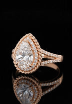 Angled top view of a pear cut engagement ring in rose gold featuring a double halo and split shank band reflecting on a black surface.