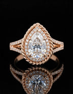 Front-facing view of a sparkling pear-shaped rose gold engagement ring with a twisted rope halo design and reflections on a dark surface.