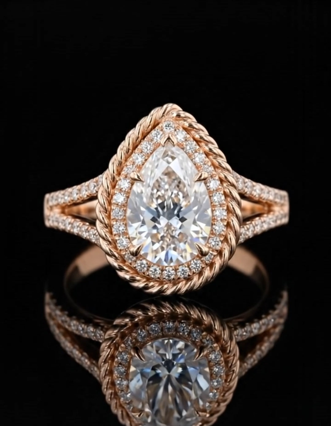 Front-facing view of a sparkling pear-shaped rose gold engagement ring with a twisted rope halo design and reflections on a dark surface.