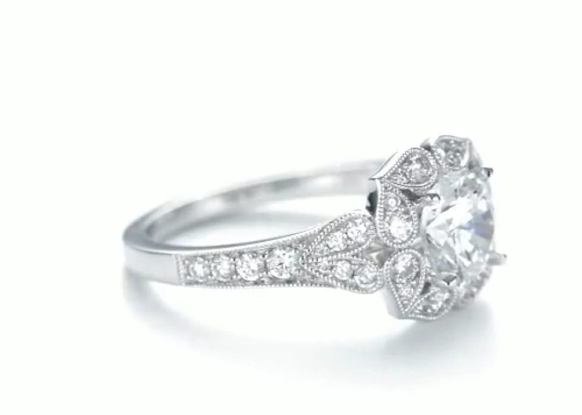 Side perspective view of white gold 2 carat round lab diamond ring showing petal halo and leaf motif shoulder
