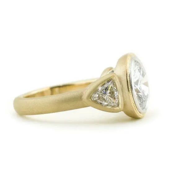 Side profile view highlighting trillion side stone in bezel setting and matte gold finish.