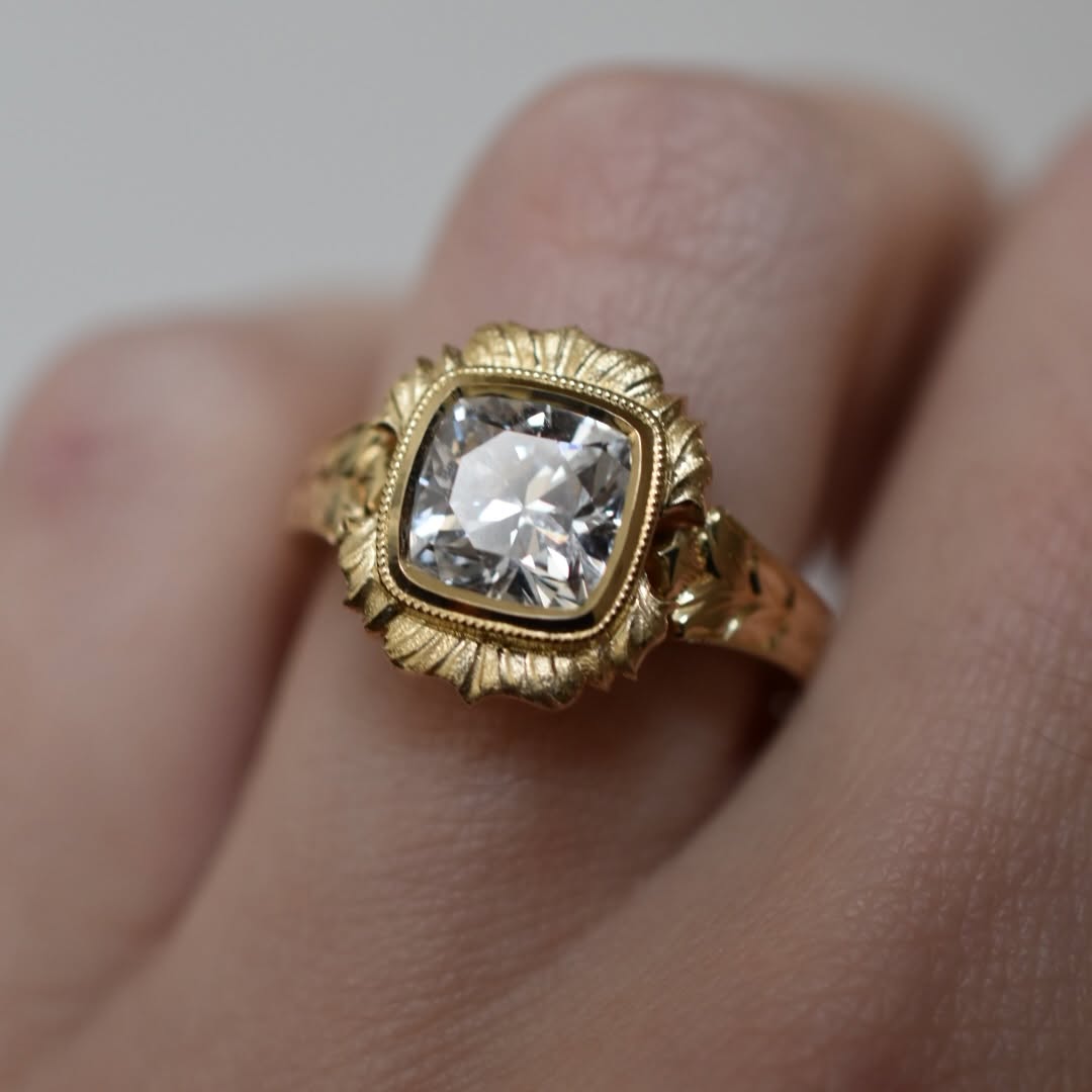 On-hand close up of a 4 CT cushion cut lab diamond ring in scalloped bezel yellow gold setting.