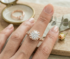 Lifestyle shot of a woman wearing a vintage-style rose gold engagement ring on her finger, with an open vintage ring box in the softly blurred background.