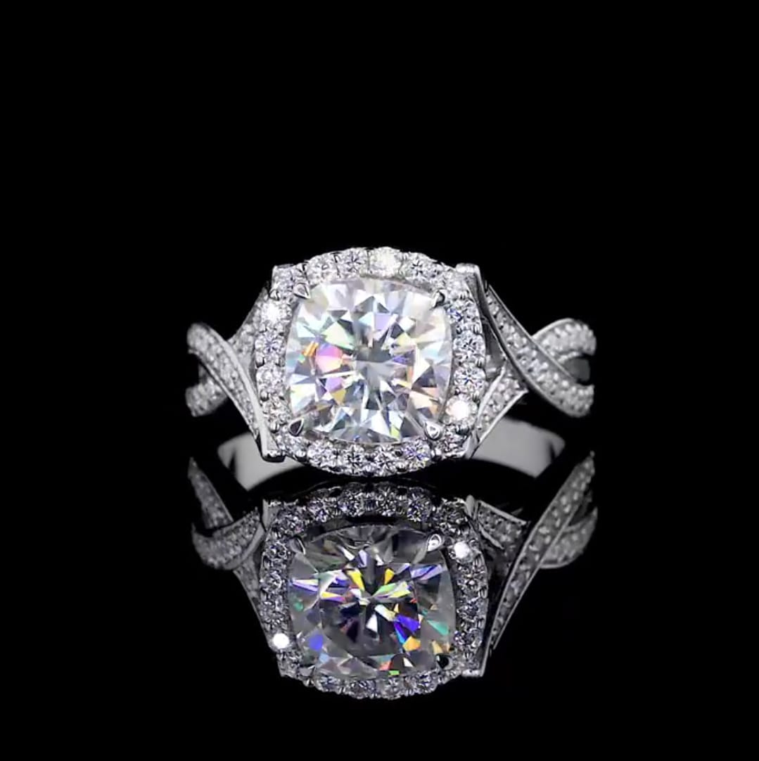 Top-down view of a 2 CT cushion cut lab grown diamond ring with a halo and twisted band, reflected on a black surface.