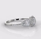 Side angle view of a white metal 2 CT round lab grown diamond ring showing a pear side stone with a halo and pave band.