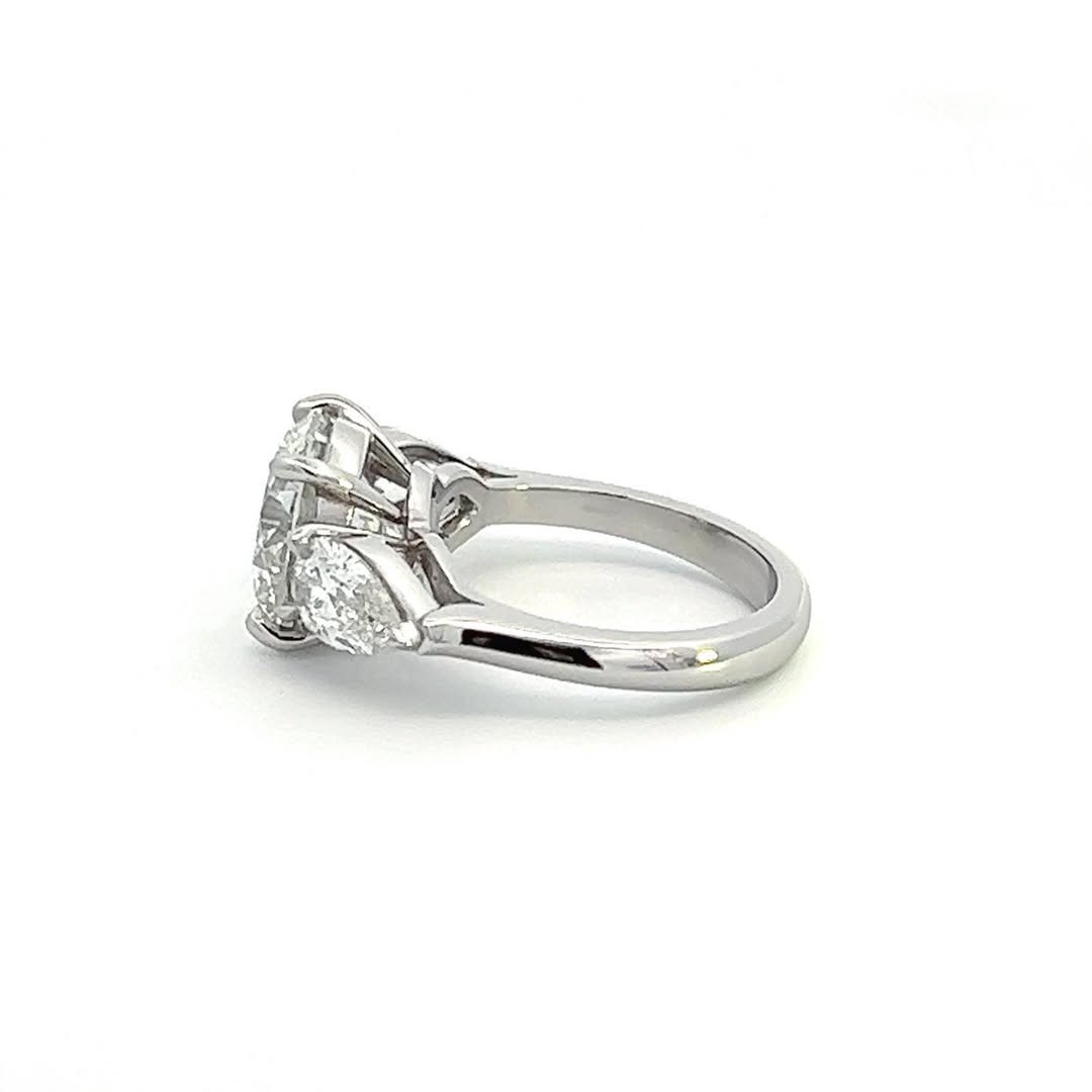 Side profile view of a 3 carat round and pear three-stone lab grown diamond engagement ring with a smooth polished band.