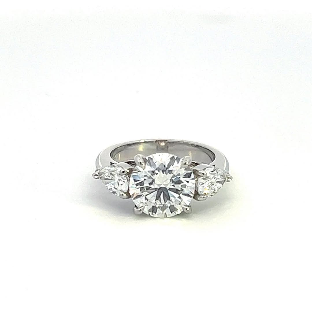 Top-down view of a stunning 3 CT round cut lab grown diamond ring flanked by two pear-shaped side stones.