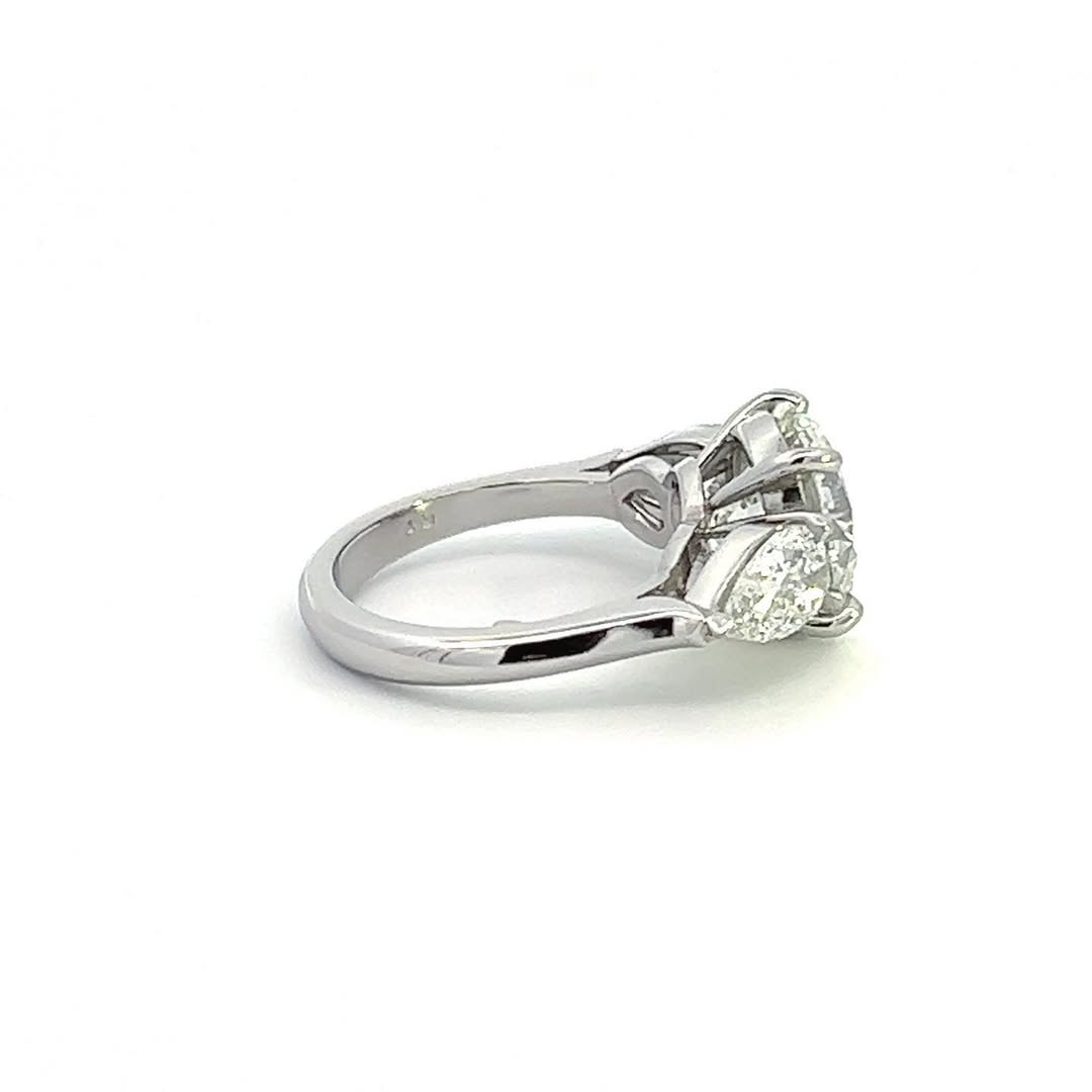 Angled side view of a classic three-stone engagement ring with a round center diamond and polished cathedral setting.