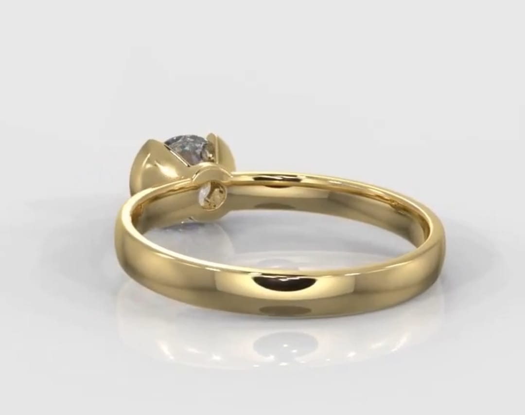 Low angle view of a 1.5 carat round cut diamond in a yellow gold half-bezel solitaire setting.