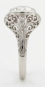 Side profile of a vintage filigree bezel engagement ring with a 3 CT oval lab diamond and chevron engraved band.