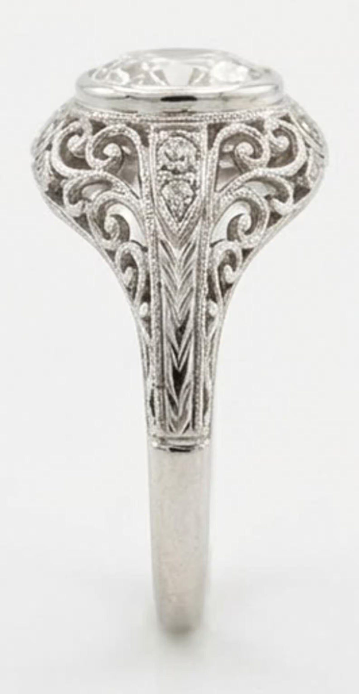 Side profile of a vintage filigree bezel engagement ring with a 3 CT oval lab diamond and chevron engraved band.