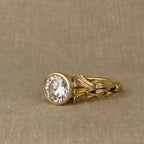 Close-up of side carved leaf texture on a yellow gold 2 CT round diamond bezel setting.
