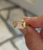 Close-up of hand holding a 3 CT pink emerald cut lab grown diamond ring in an East-West yellow gold bezel setting.