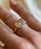 Top-down view on finger of horizontal 3 CT pink lab diamond engagement ring in yellow gold.