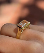 Perspective side view of East-West pink emerald cut bezel set diamond ring on hand.