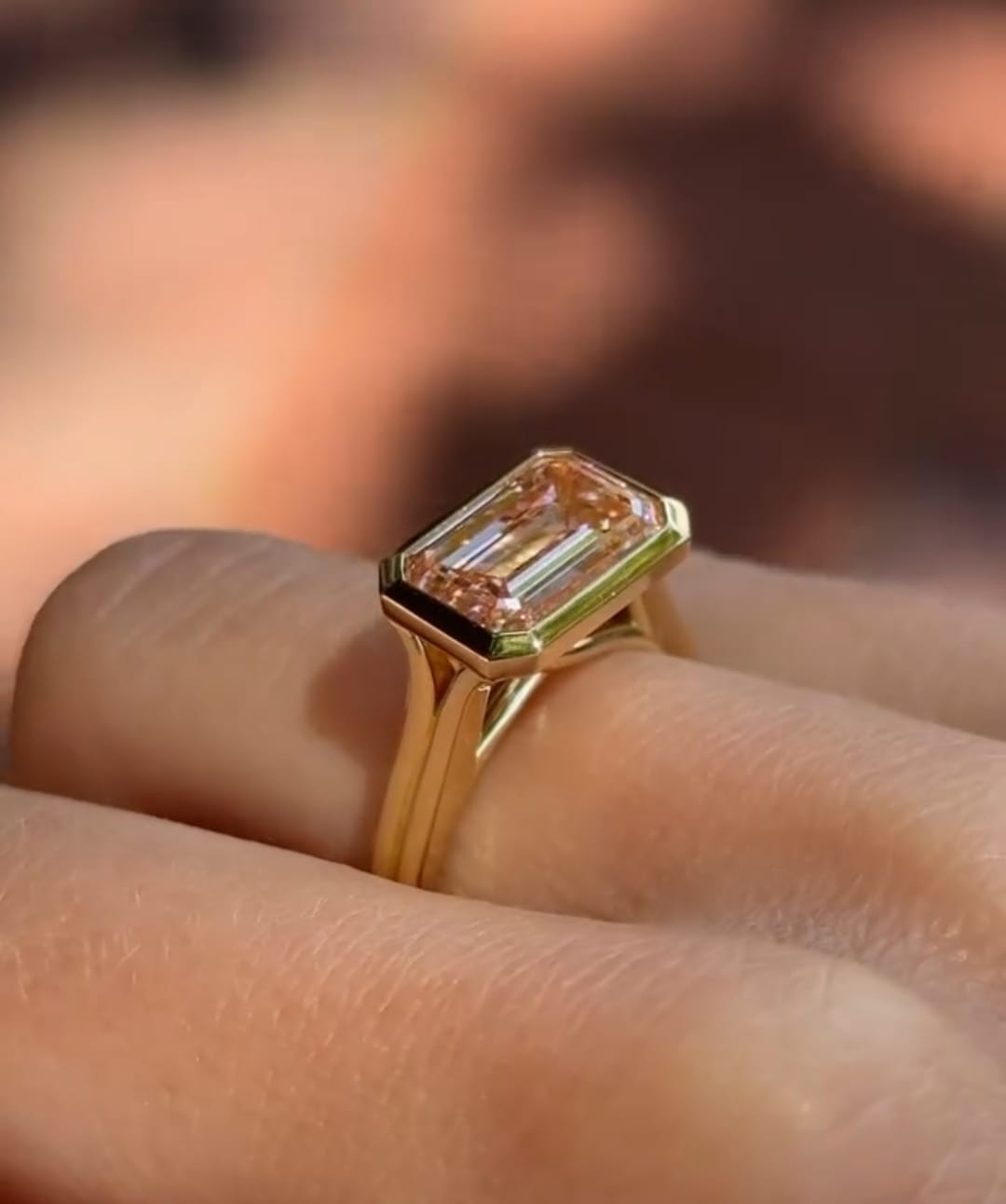 Perspective side view of East-West pink emerald cut bezel set diamond ring on hand.