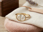 3 carat oval lab grown diamond bezel ring with pavé diamond band resting on fabric display.