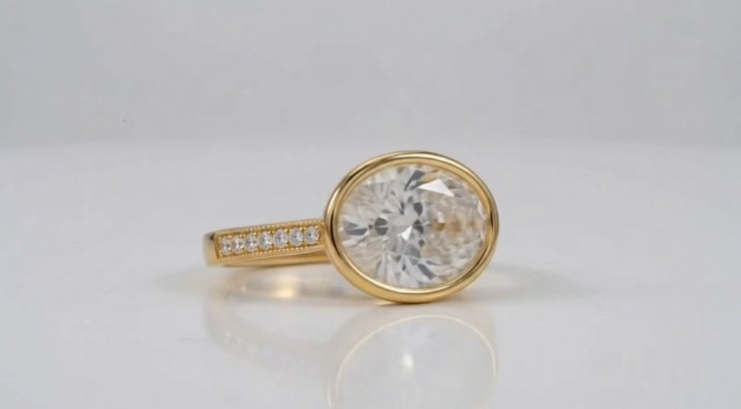 Horizontal 3 CT oval lab diamond ring with milgrain pavé accent band in yellow gold.