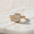 Front view of a 3ct elongated radiant cut lab grown diamond engagement ring with a milgrain bezel and engraved band resting on white marble.