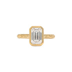 Top view of yellow gold 3 CT emerald cut lab diamond ring featuring milgrain bezel and floral engraved shank.