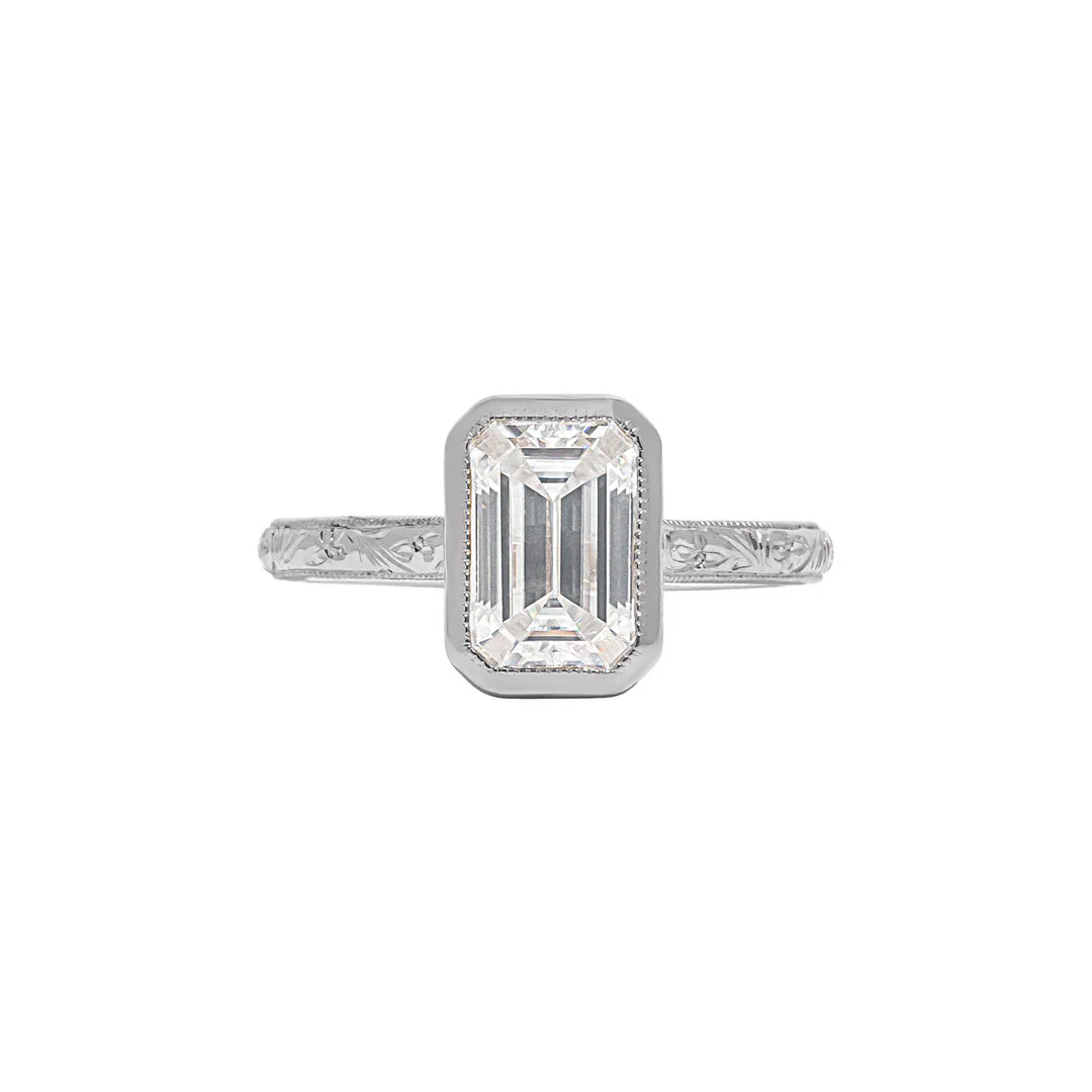 Top perspective of white gold 3 CT emerald cut lab grown diamond bezel ring with hand-carved vintage pattern.