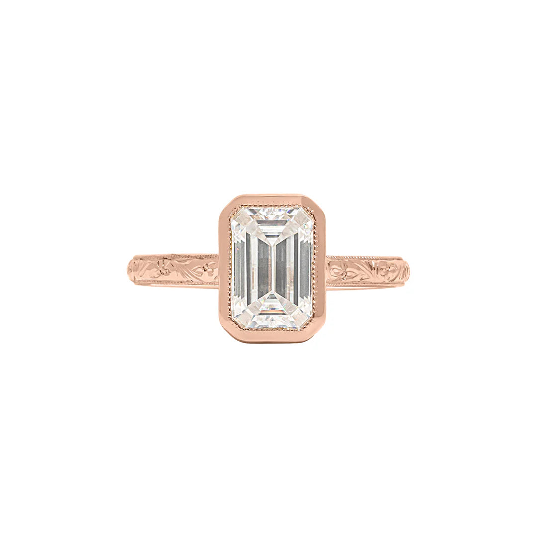 Top view of rose gold 3 CT emerald cut lab diamond ring with protective bezel setting and engraved detailing.