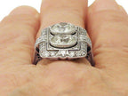 Close-up view on finger showing dual bezel-set round lab diamonds and intricate milgrain surface detail.